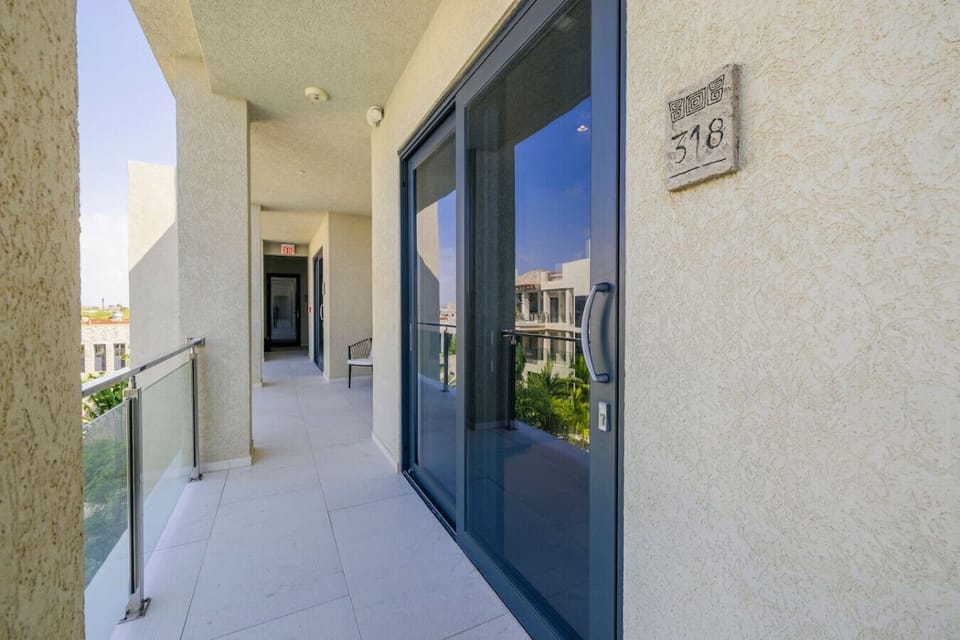 A view down a clean, well-lit apartment corridor with a glass door to a private balcony. The building’s exterior is simple and elegant, with light-colored walls and a modern design.