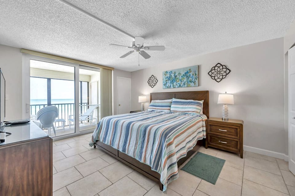 Serene bedroom w/ a cozy bed, beach-inspired accents, and balcony access for easy mornings.