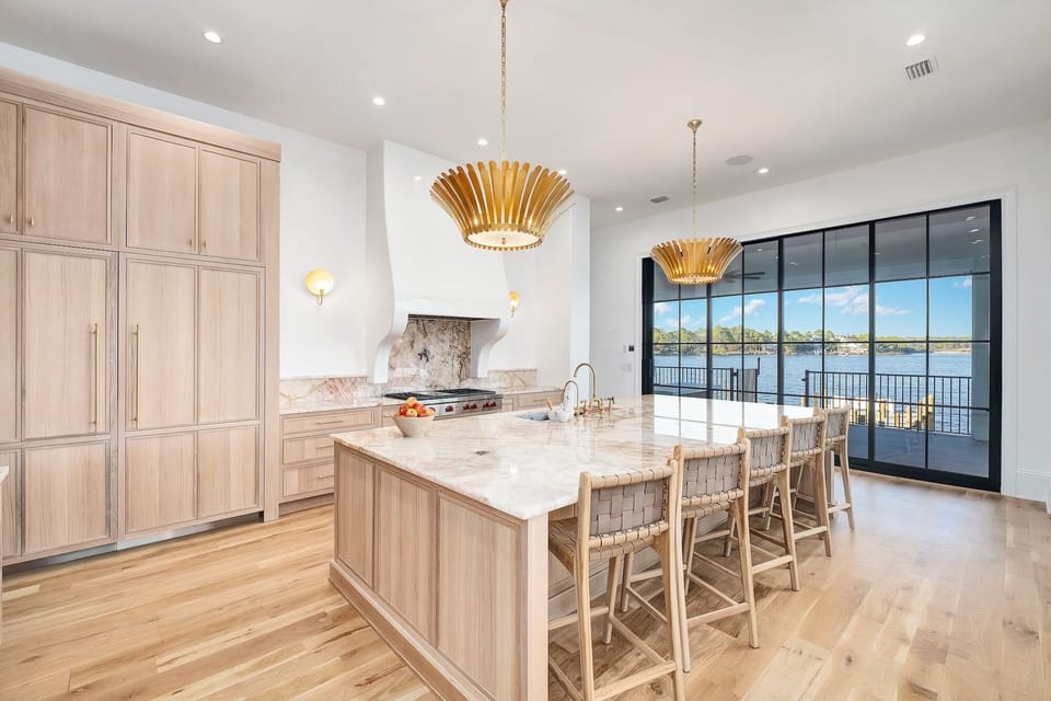 Your gourmet kitchen features marble countertops, warm wood cabinetry, and stunning water views through floor-to-ceiling windows.