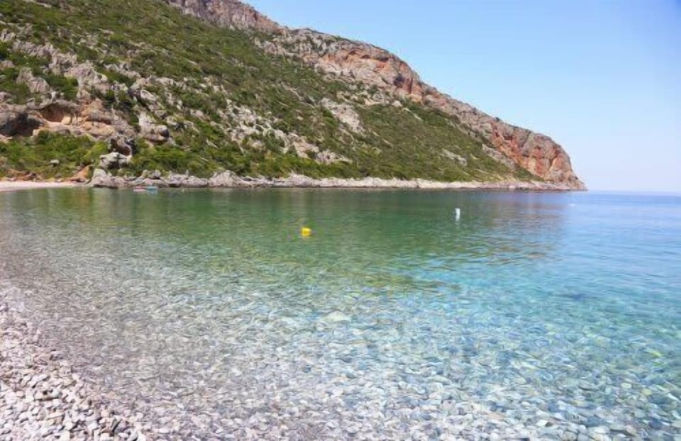 A serene pebbled beach with crystal-clear water, perfect for a refreshing swim.

