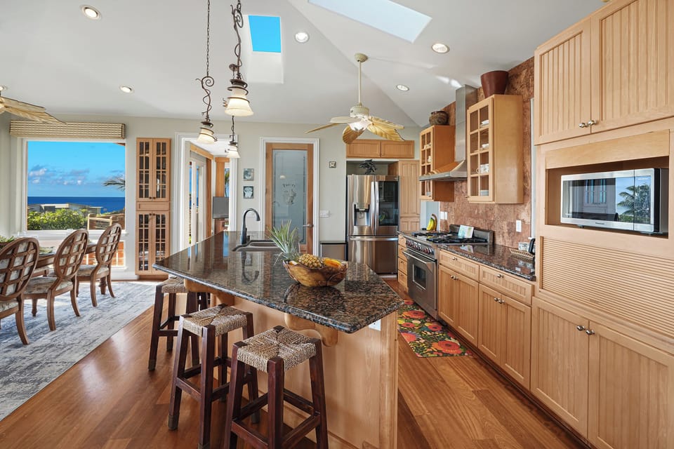 Spacious sunlit kitchen, granite island, bar stools, stainless, wood, skylights
