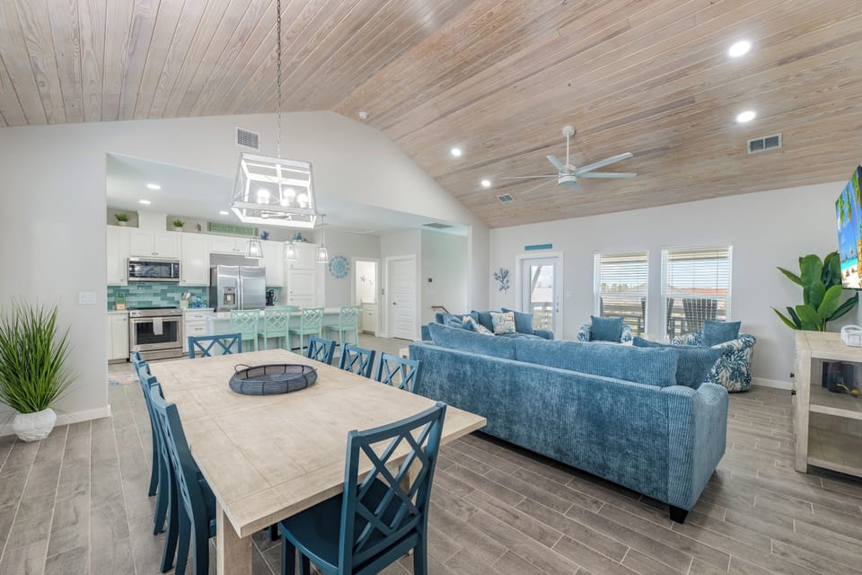 Relax in your stunning open-concept living space featuring coastal-inspired design, soaring wood ceilings, and seamless flow between kitchen, dining, and living areas.