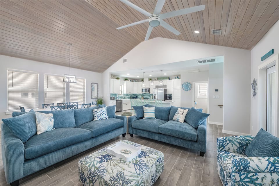 Sink into plush coastal sofas and feel the ocean breeze from your ceiling fan in this stunning open-concept retreat.