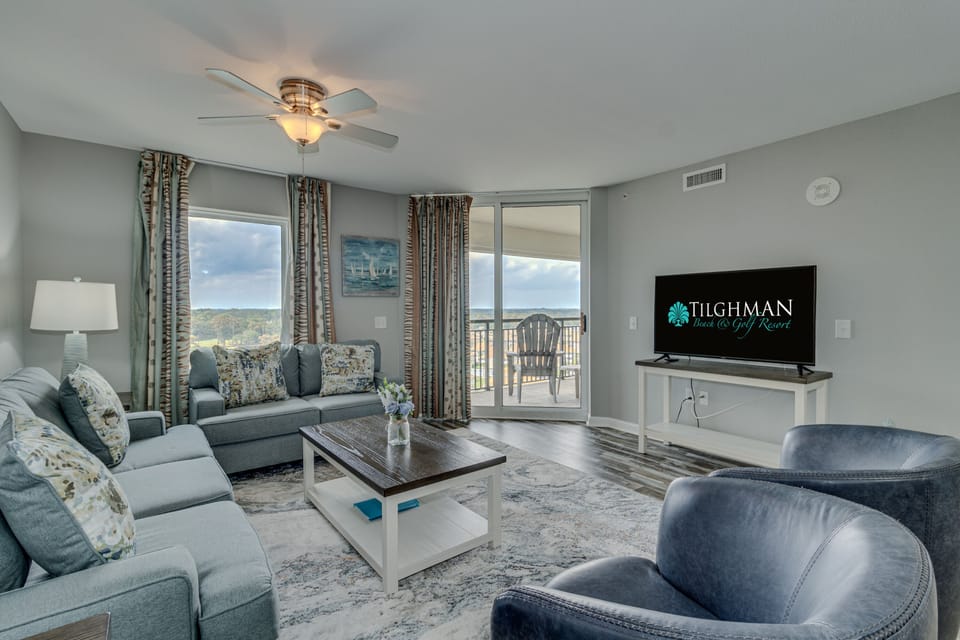 Relax in your spacious living room with comfortable seating, ceiling fan, and sliding doors opening to your private balcony with scenic views.