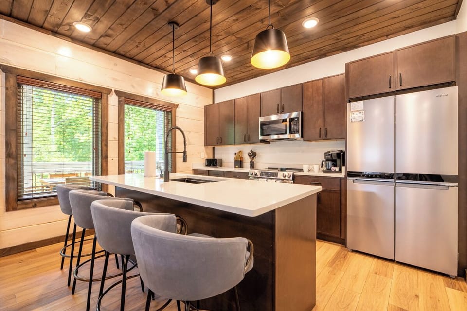 Gather around your spacious kitchen island with modern appliances, warm wood tones, and sunlight streaming through the windows—perfect for morning coffee or meal prep with friends.