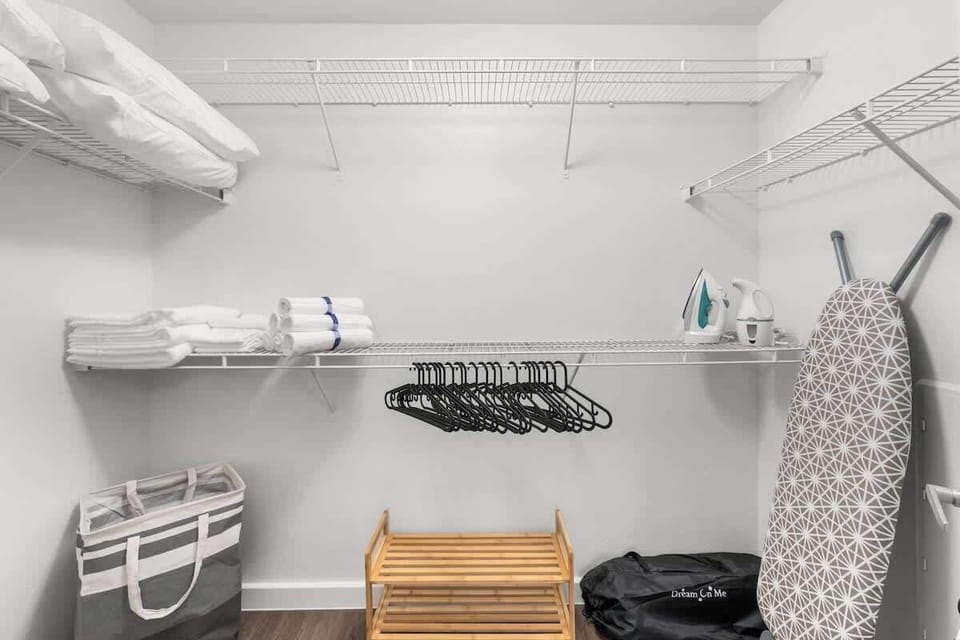 A large closet with plenty of storage space for clothes, hangers, steamer, shoe rack, and extra air mattress