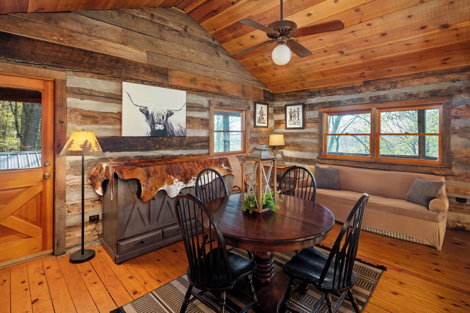 Cozy 4th-floor loft with rustic charm, warm wood accents, treetop views, a stylish dining area, plush sofa, and a queen-size Murphy bed. Perfect spot for family meals or game nights in this inviting mountain cabin retreat.