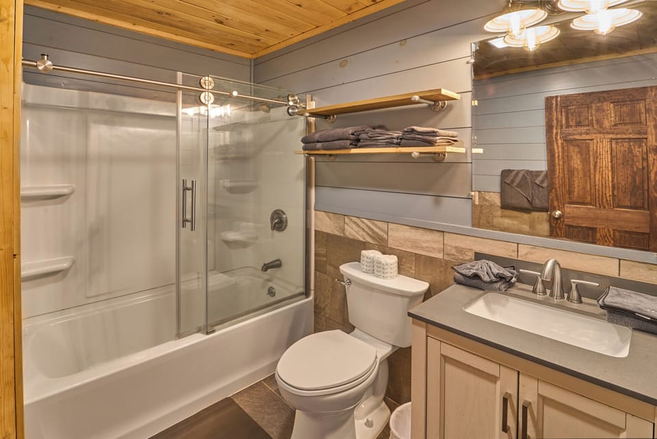 Clean bathroom featuring a glass-enclosed tub, modern fixtures, and stocked with essentials.