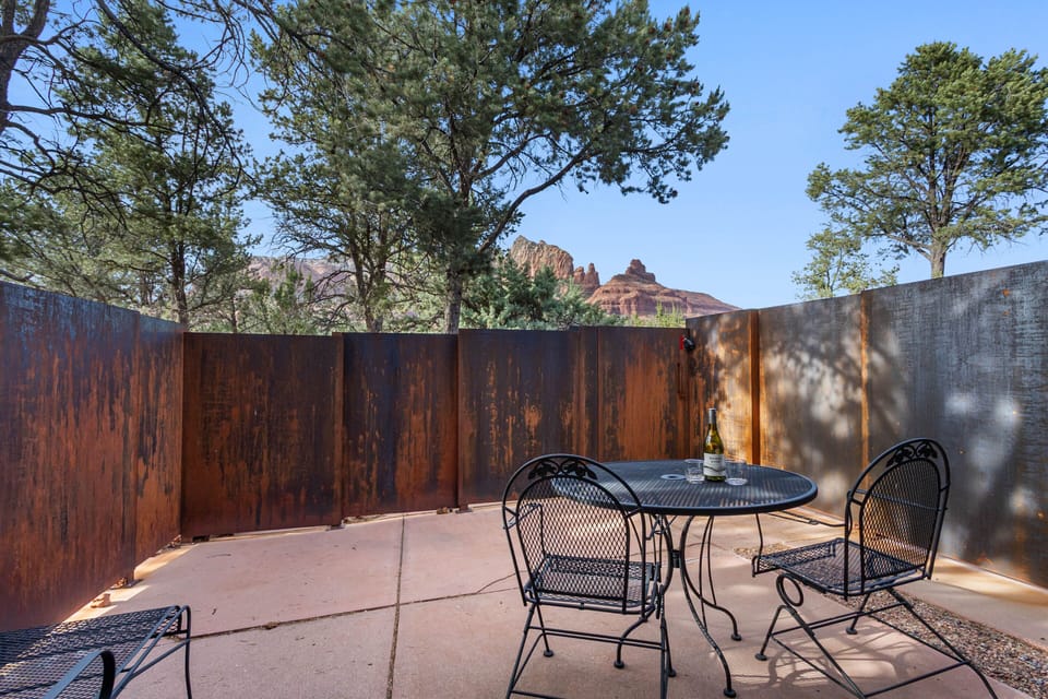 Patio with slight red rock view, table with seating for two, one lounge chair.