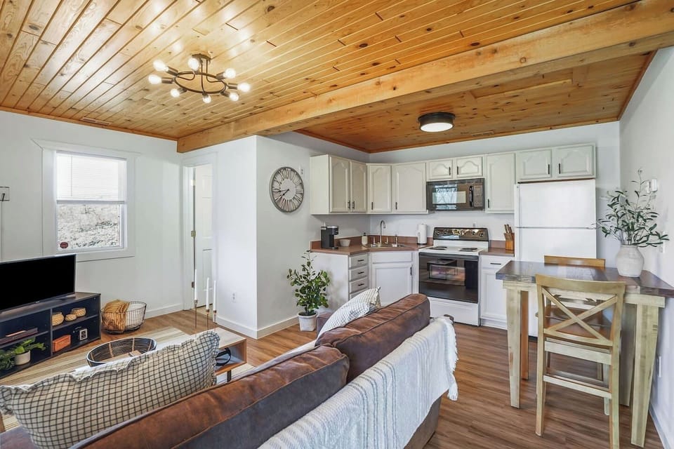 This open living space features a cozy sofa, wood-paneled ceiling, and a fully equipped kitchen with dining area. Bright and welcoming, it’s the perfect spot to cook, relax, and spend time together in comfort.