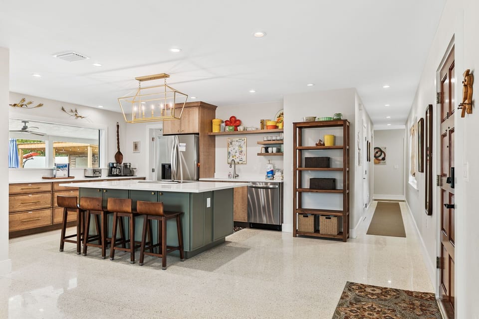 Step into your stunning open-concept kitchen where warm wood and sage green create the perfect cooking sanctuary. Pull up a leather stool at the spacious island and let the coastal breeze flow through while you craft memories.