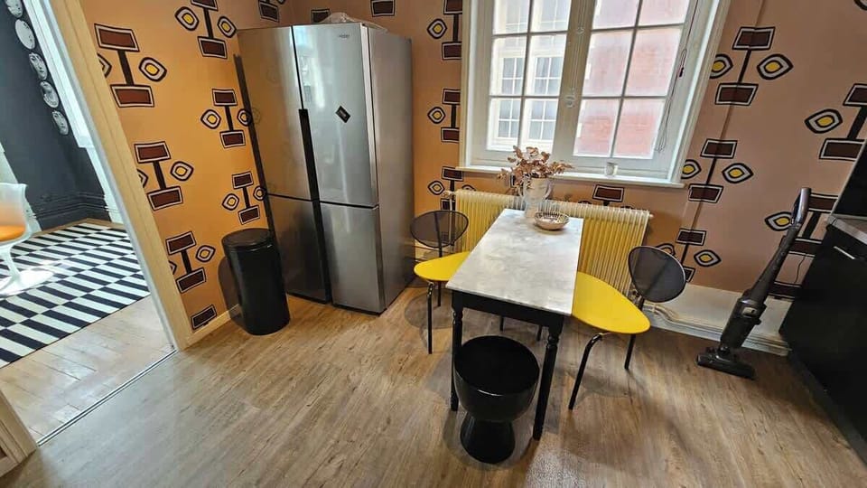 Coin repas pour trois personnes dans la cuisine équipée avec machine à café, bouilloire, grille-pain, micro-ondes, plaques de cuisson, four, lave vaisselle et réfrigérateur avec congélateur.