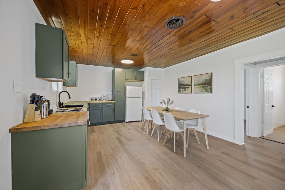 Modern kitchen with green cabinets and a dining area for six under a warm wooden ceiling