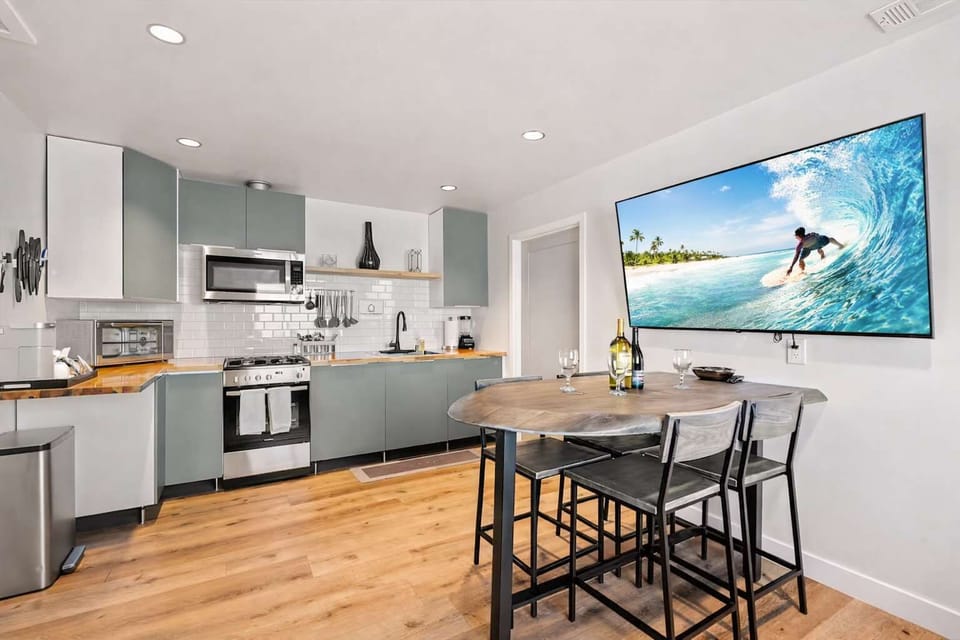 Bright Open-Concept Living Room with Sofa Bed, Modern Kitchen, and Large TV — Clean Coastal Design for Relaxed Stays

