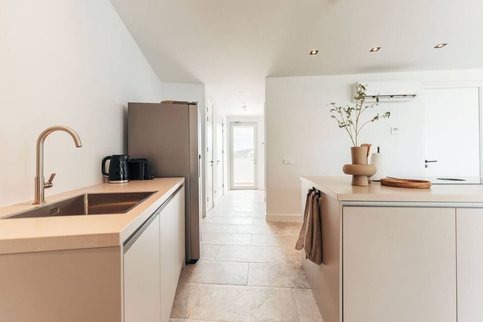 A modern kitchen with a clean, minimal aesthetic. The simple yet elegant design features a streamlined sink area, stainless steel fridge, and soft lighting for a bright, airy space.