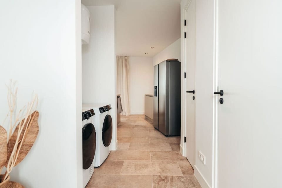 A clean, functional hallway featuring modern laundry machines and a sleek refrigerator. The minimalistic design and neutral tones keep the space organized and clutter-free.