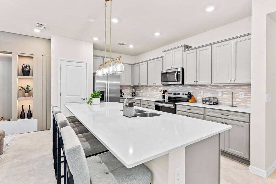 Discover culinary delights in our stylish kitchen with elegant gray cabinetry and a stunning white quartz countertop. The spacious island with bar seating is ideal for gatherings, while pendant lighting adds a warm, inviting.