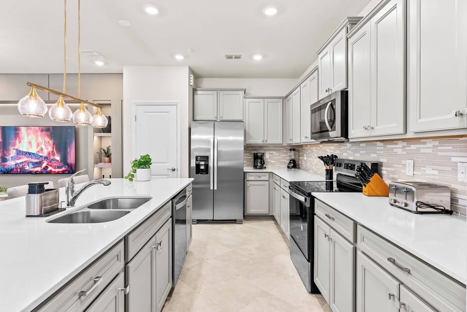 Welcome to a bright kitchen with sleek gray cabinets and a spacious white countertop, ideal for meal prep. Enjoy the warm ambiance from stylish pendant lights and a cozy electric fireplace as you savor your delicious creations.