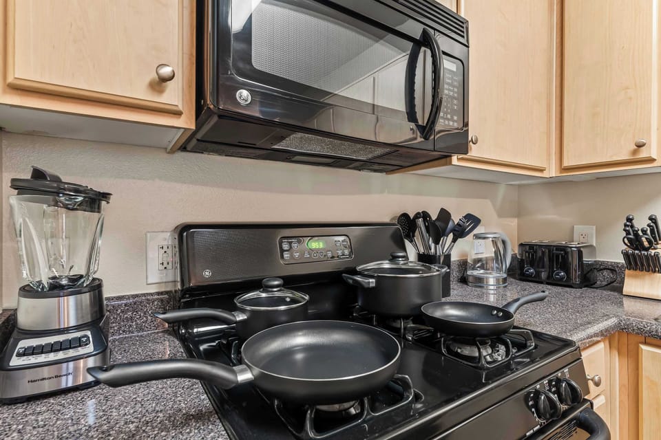 The cooking area featuring a microwave, gas stove, and blender, with all essential cookware neatly arranged.