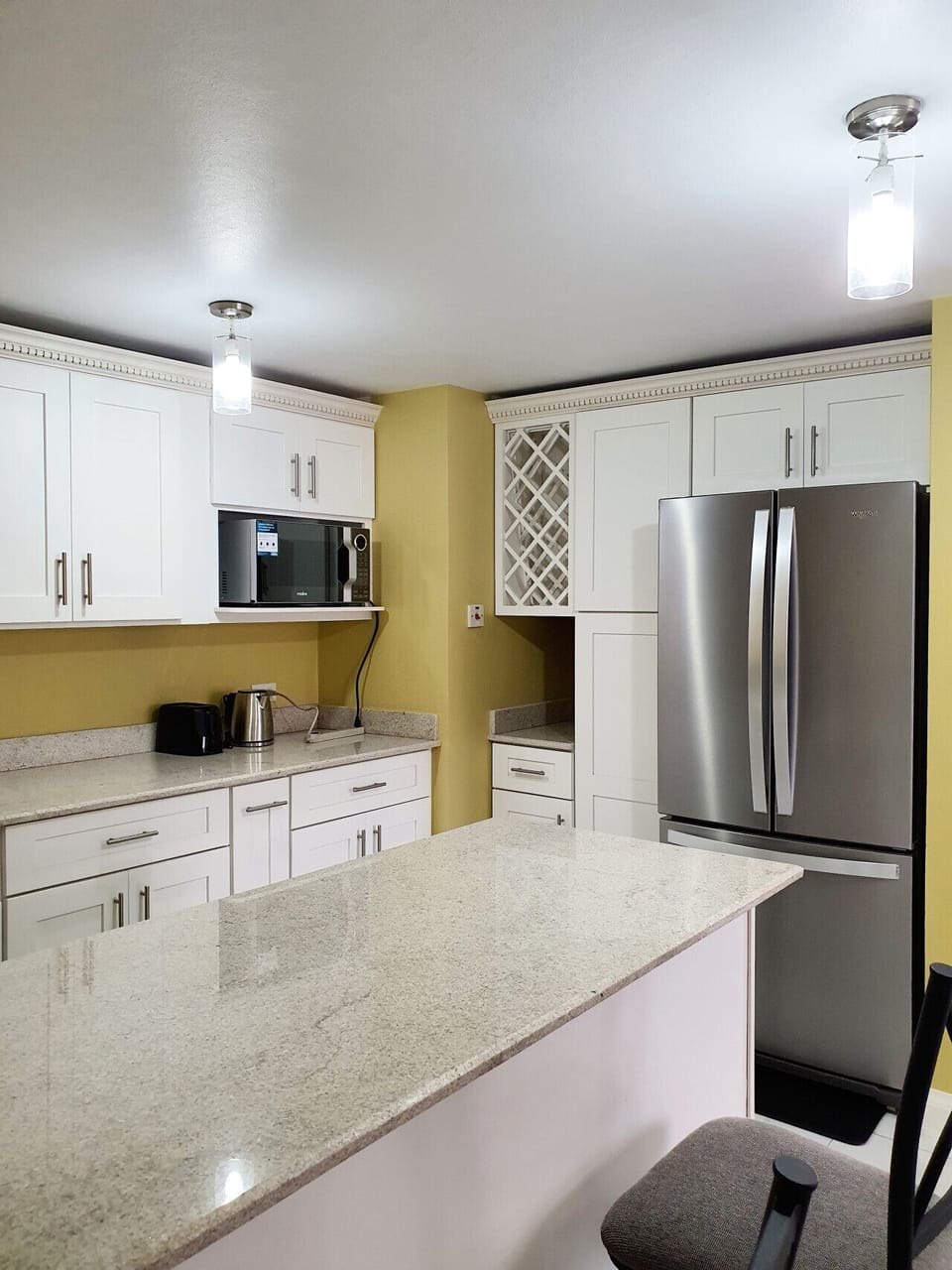 Bright kitchen w/ white cabinets, microwave, toaster & stainless fridge.