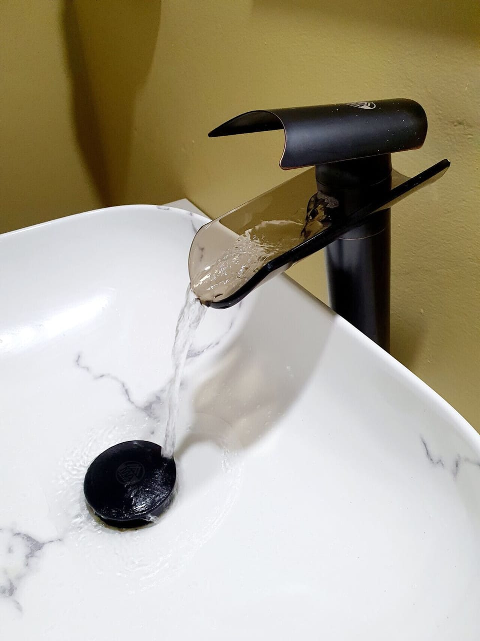 Close-up of the sleek faucet pouring water into the marble-style vessel sink.