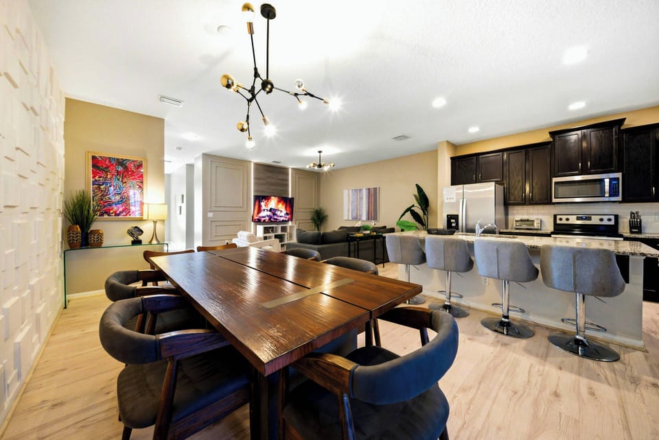 Enjoy a chic dining area with a beautiful wood table for six and cozy modern chairs, alongside a kitchen with sleek dark cabinets and contemporary appliances, all illuminated by warm, welcoming light.