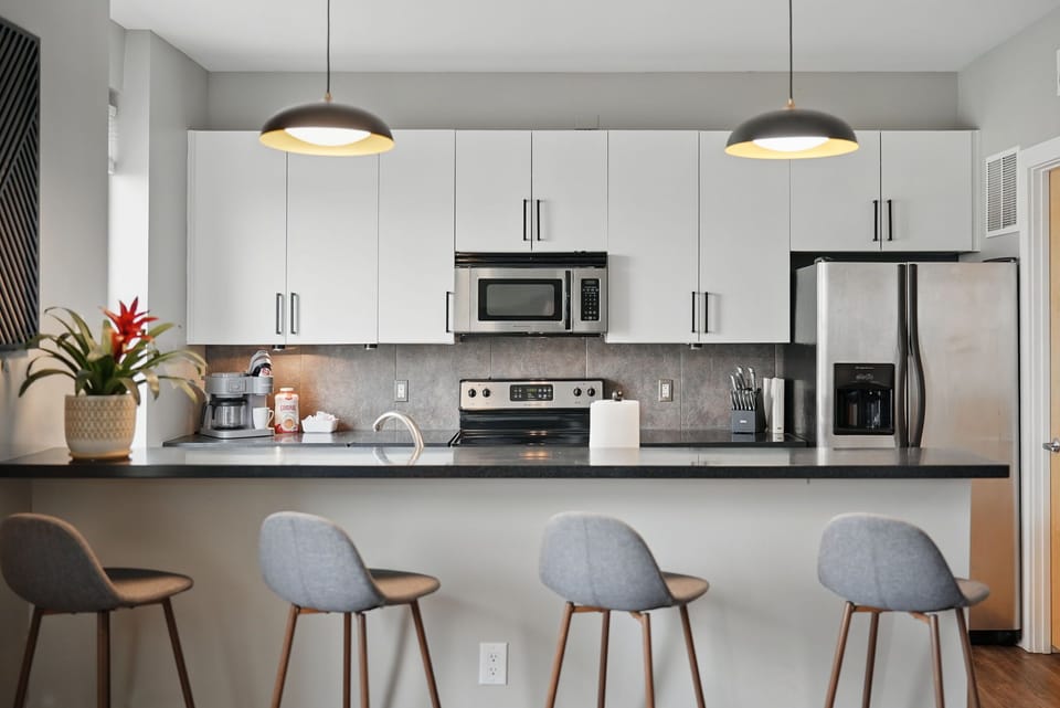 Fully stocked kitchen with stainless appliances, coffee maker, and sleek bar seating for four. Ideal for cooking, working remotely, or enjoying takeout with style.