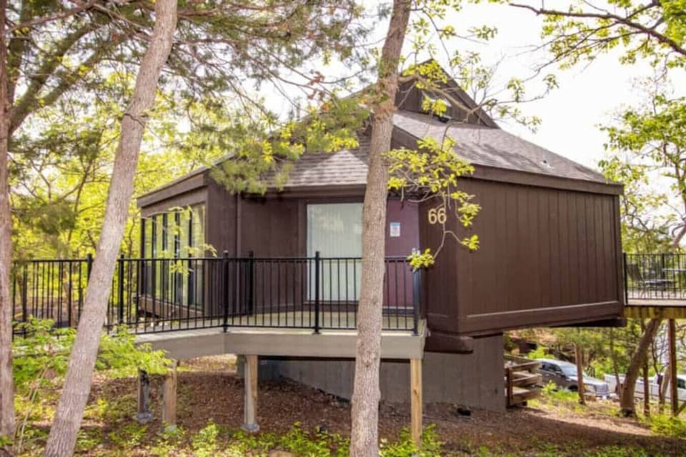 A cozy treetop cabin, nestled in a wooded area, featuring an elevated entrance with a black metal railing for a peaceful nature retreat
