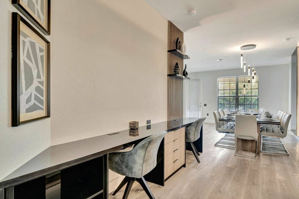 A sleek workspace combines functionality with style, featuring a polished surface and stylish chairs. Natural light floods the adjacent dining area, creating a warm atmosphere perfect for meals or casual gatherings.