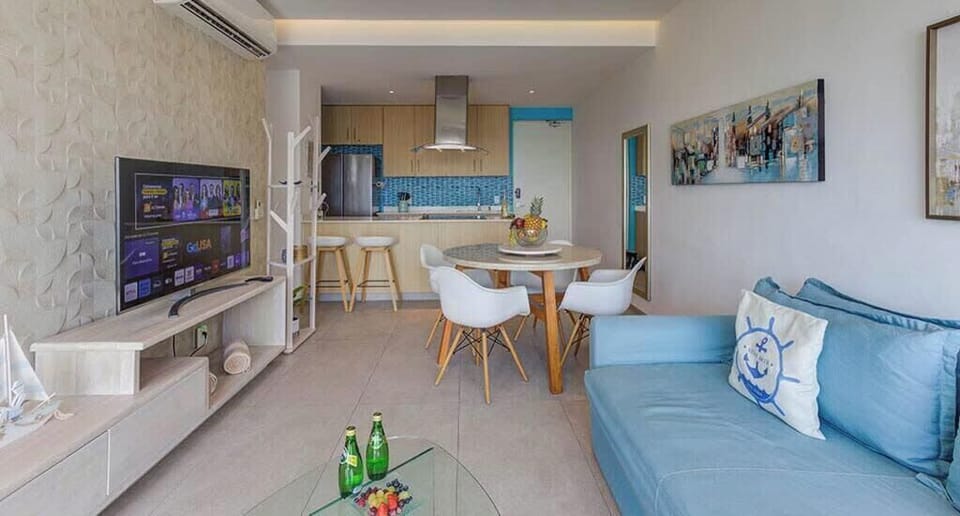 Bright living area w/ wall-mounted TV, dining table & inviting blue sofa seating