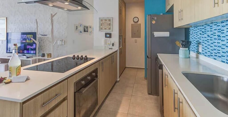 Bright kitchen workspace w/ long counters, cooktop & stylish blue backsplash