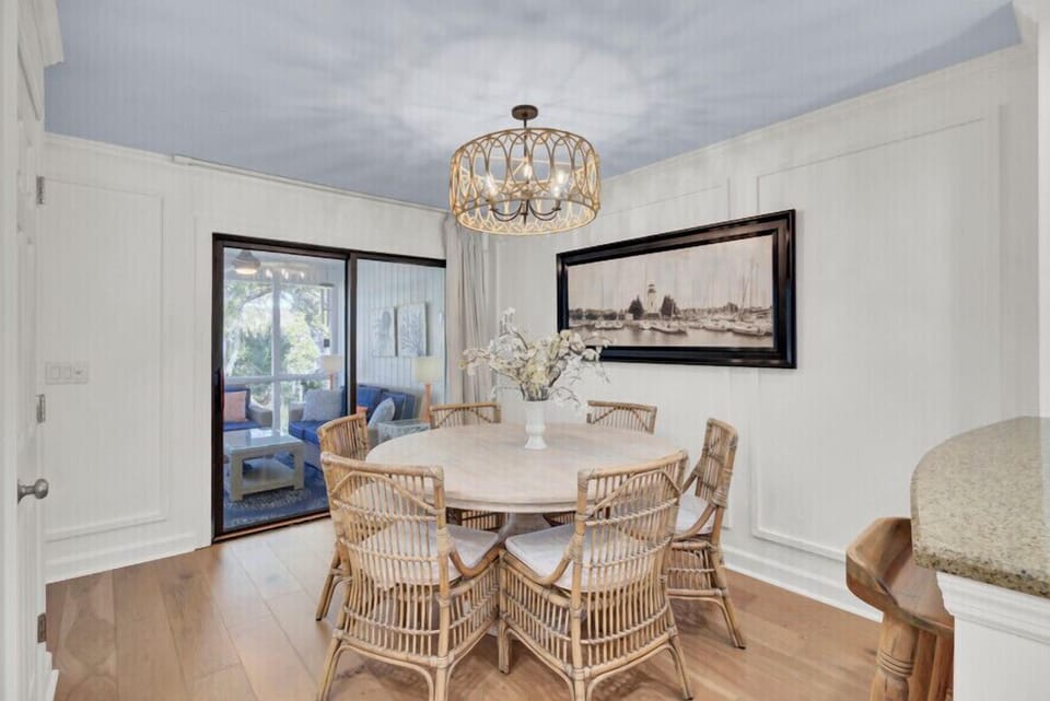 Gather around this elegant dining table for memorable meals with your group. Natural light streams in through glass doors, while coastal artwork and a statement chandelier add charm to your dining experience.