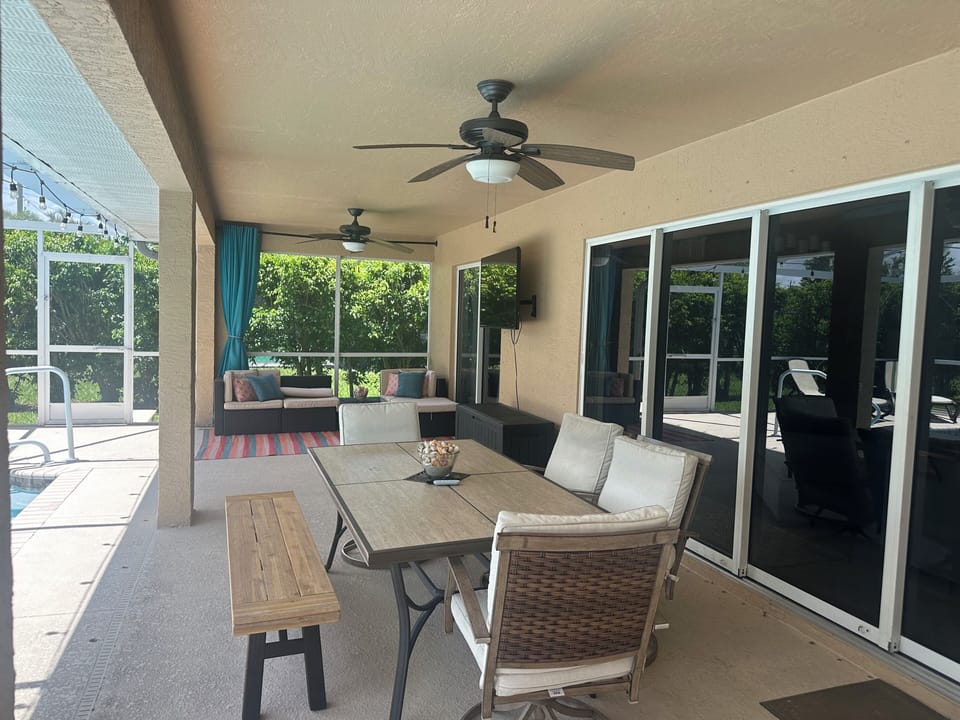 Screened lanai with outdoor dining table and seating, overlooking the pool and backyard