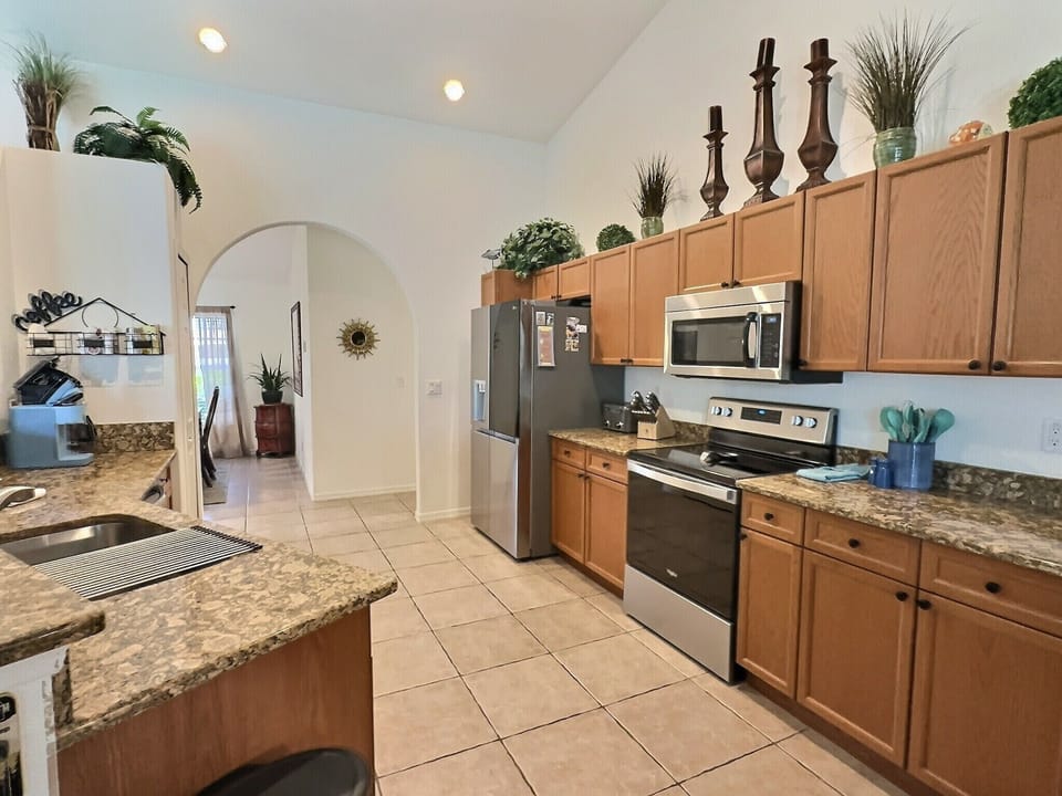 Kitchen with wood cabinetry, stainless steel appliances, granite countertops, and tile flooring