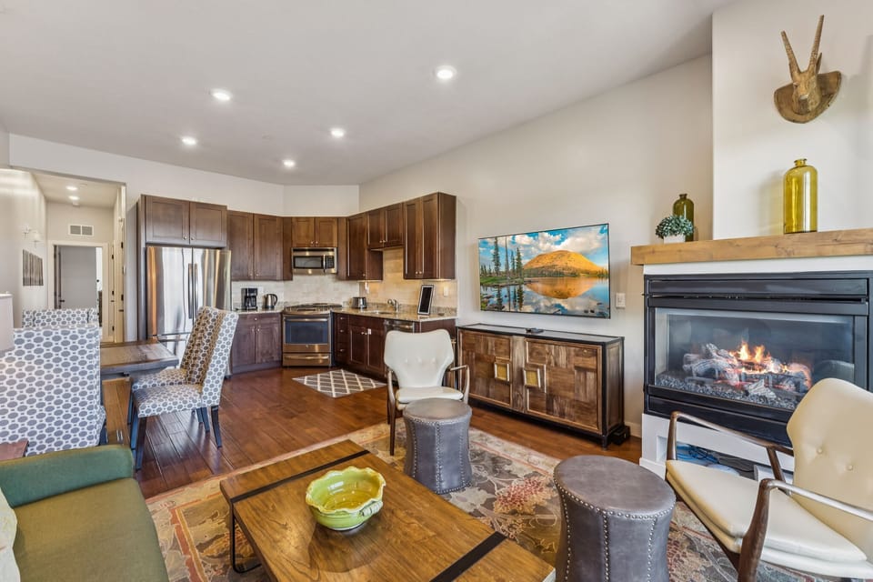 Cozy and stylish open-concept living space featuring a modern kitchen, inviting fireplace, and comfortable seating—perfect for relaxing after a day of adventure.