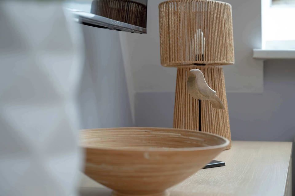 A wooden floor lamp with a woven shade, placed next to a wooden stool. 