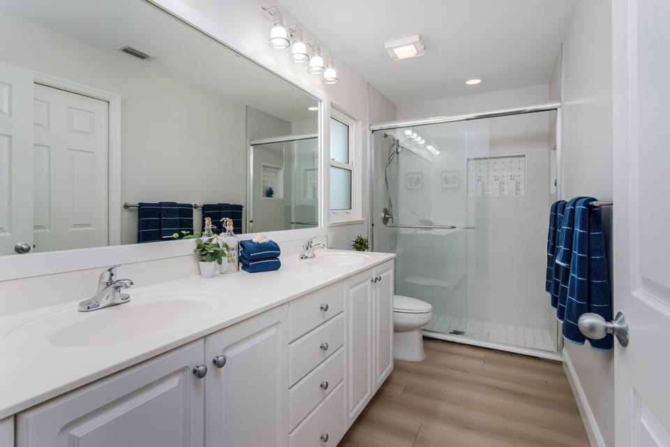 Step into your private spa-like retreat where crisp white vanities and gleaming fixtures await your morning routine, while the spacious glass shower promises a refreshing start to your day.
