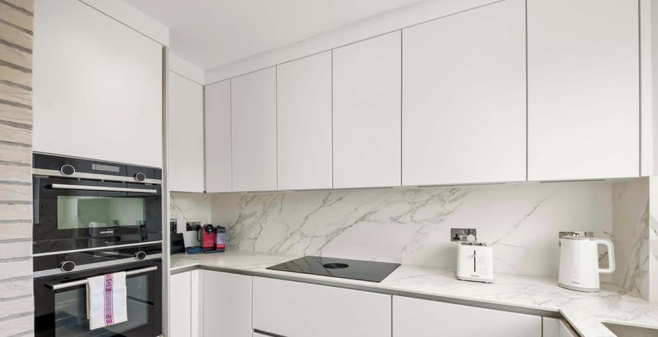 The ultra-modern kitchen features sleek handleless white cabinetry, integrated double ovens, and a luxurious marble-effect backsplash.