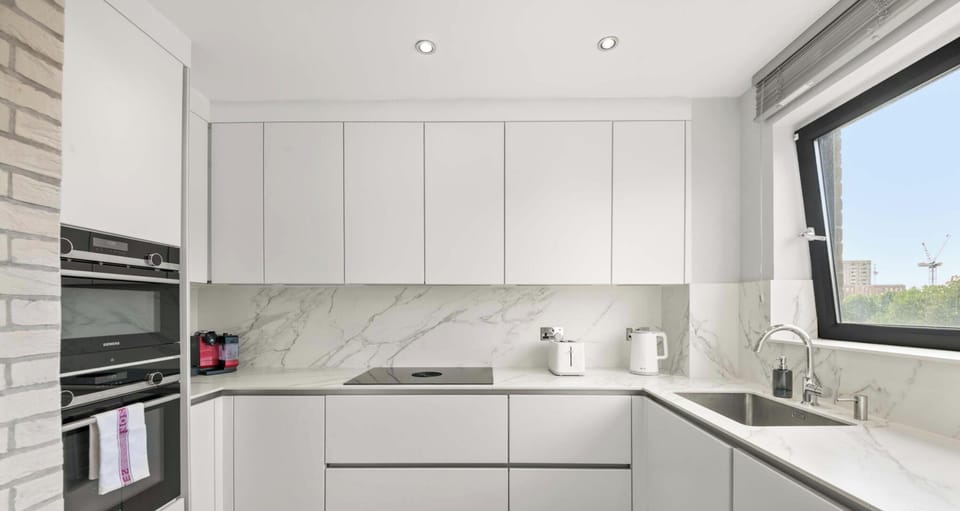 This perspective of the kitchen showcases the seamless transition between the white minimalist cabinets and the functional sink and stovetop area.