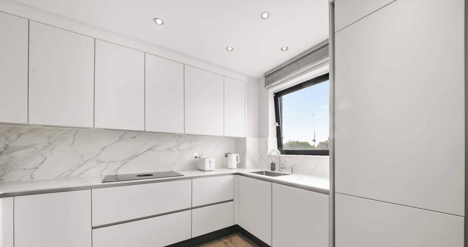 A wide-angle view of the L-shaped kitchen highlights the clean lines of the white countertops and the natural light flowing in from the large window.