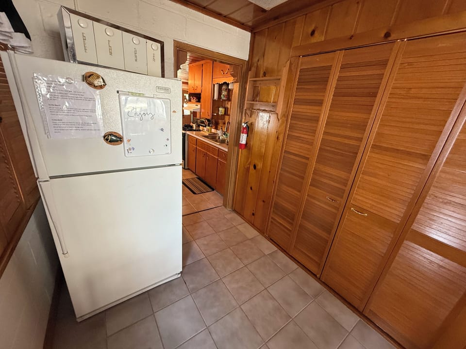 Refrigerator with laundry room behind wooden cabinets.