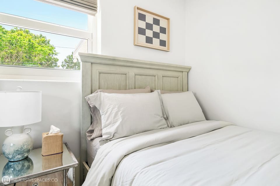 Relax in this serene bedroom, featuring a comfortable bed with elegant bedding, a stylish nightstand, and abundant natural light.
