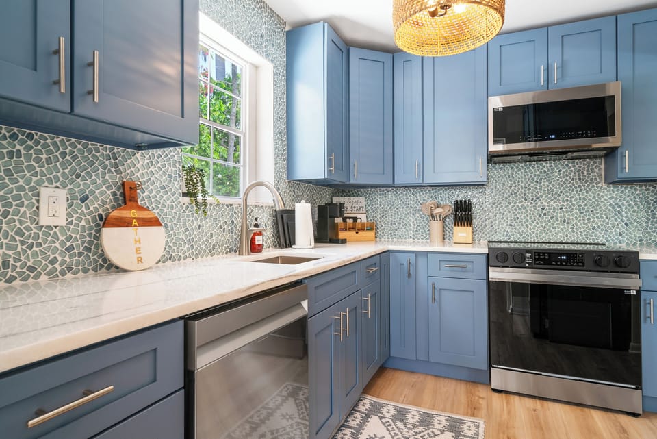 Bright kitchen with blue shaker cabinets, mosaic tile backsplash, marble counters, and stainless appliances - beautifully fresh.
