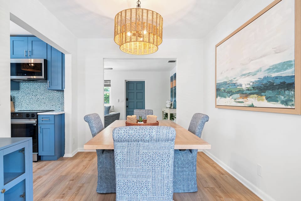 Bright dining room with rattan chandelier, wood table seating six, and blue mosaic-backsplash kitchen steps away — flow-through living at its best