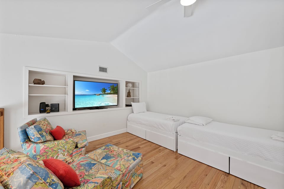 Relax in your bright bedroom featuring twin beds, built-in entertainment center, and tropical beach scenes on the large TV.