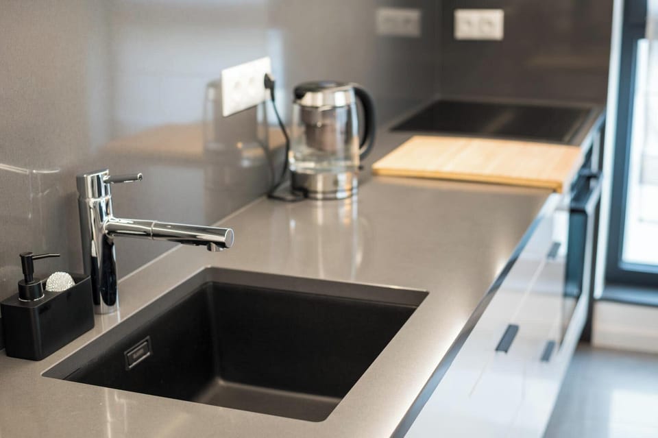 A modern kitchen sink area with stainless steel fixtures and utensils on the counter. 