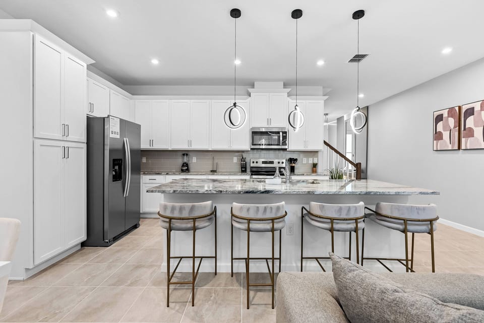 Enjoy a culinary delight in this stylish kitchen with a spacious island and chic bar stools, bright white cabinetry, and modern lighting. Sleek stainless steel appliances add both functionality and sophistication to the space.
