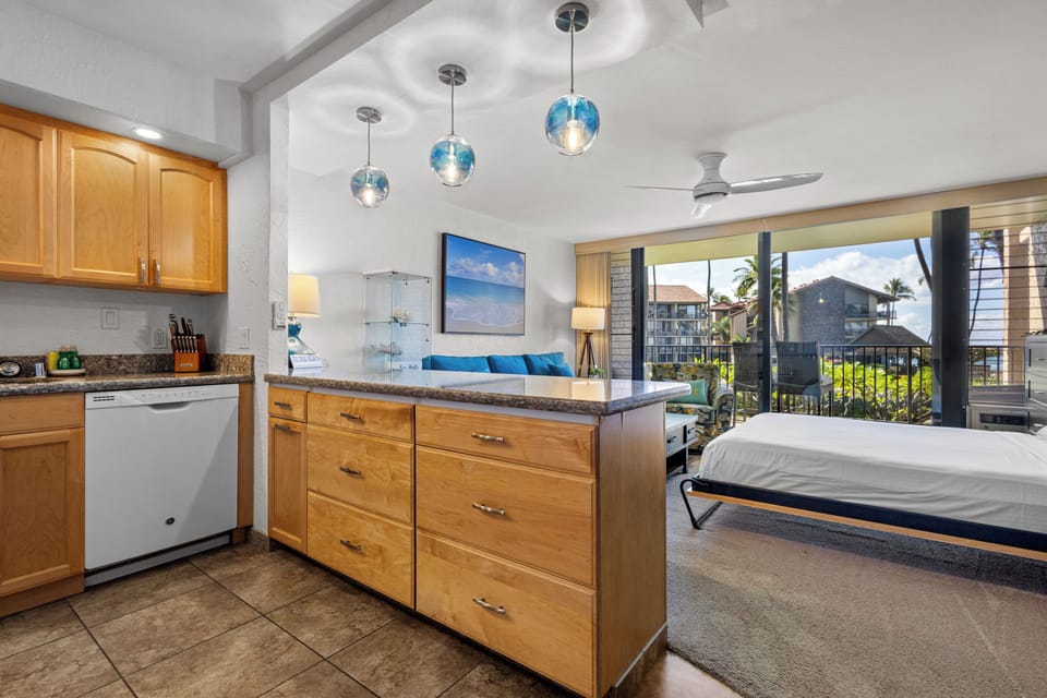Your open-concept studio blends coastal style with comfort—blue pendant lights, a fully-equipped kitchenette, and a king bed steps from your private lanai overlooking swaying palms and neighboring rooftops.