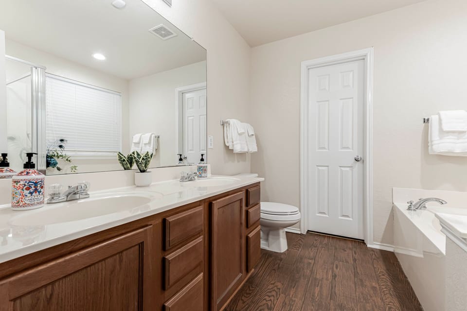 Bathroom featuring a double vanity, large mirror, toilet, and soaking tub.