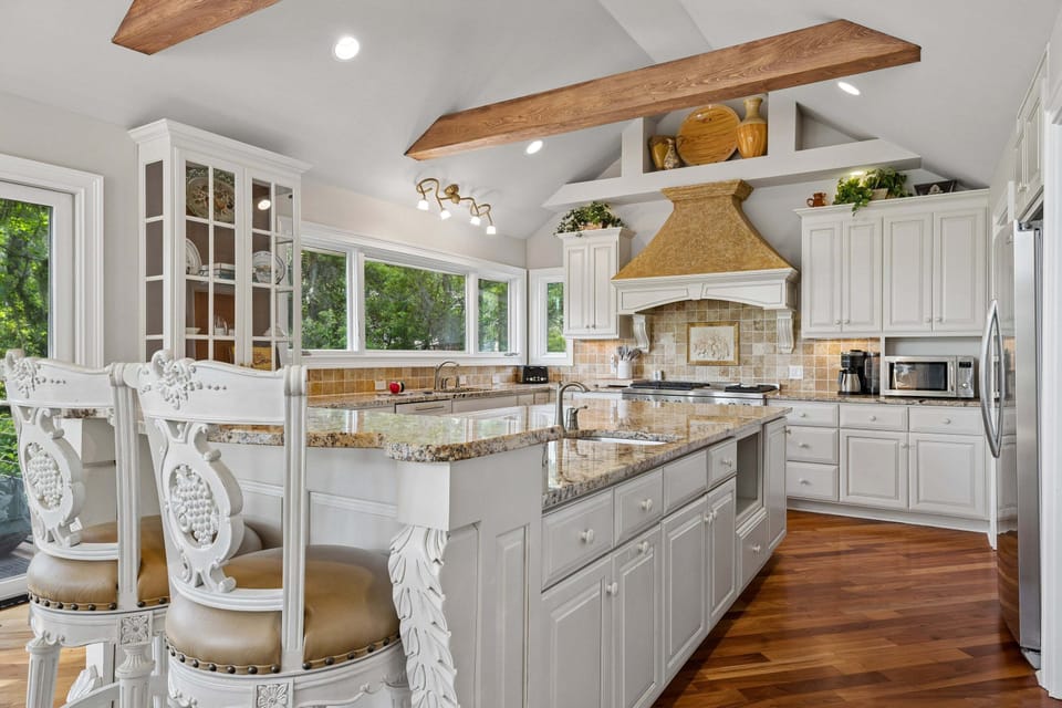 Whip up unforgettable meals in this sun-drenched gourmet kitchen featuring a grand granite island, custom range hood, and elegant glass cabinetry.